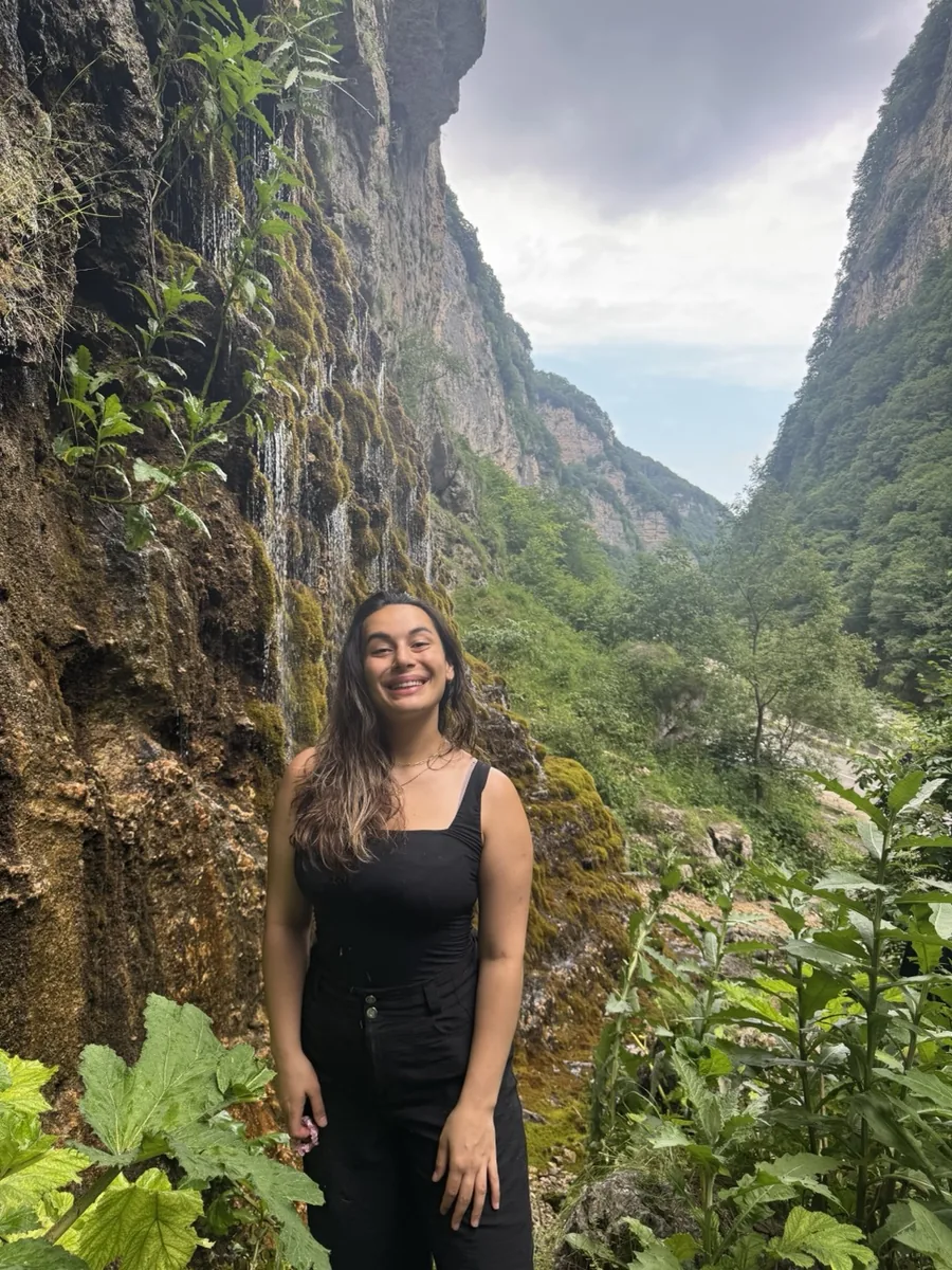 Zulia standing in front of a mossy cliff with a waterfall